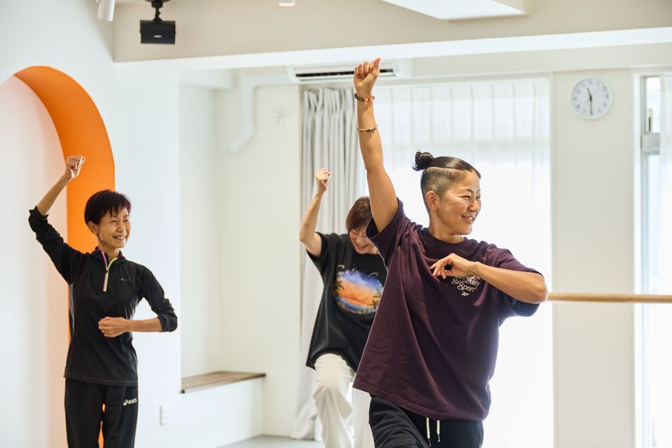 スタジオで、会員の皆さんが講師と一緒に腕を上げて踊っている様子